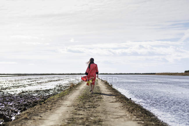 Vista trasera de joven mujer asiática en pista de tierra por mar en ropa tradicional - foto de stock