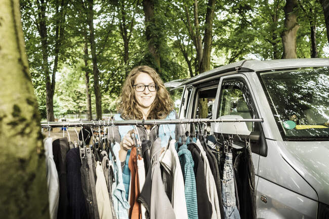 Portrait of female stall holder by second hand clothes rail at forest flea market — Stock Photo