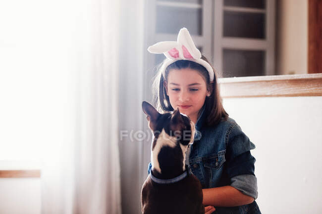 Дівчина сидить з собакою, в приміщенні, дівчина в великодніх вухах кролика — стокове фото