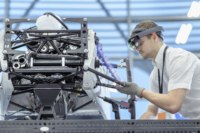 Engineer using augmented reality headset to 'see' parts position on car in assembly composite image showing CAD drawing of part in robotics research facility — Stock Photo