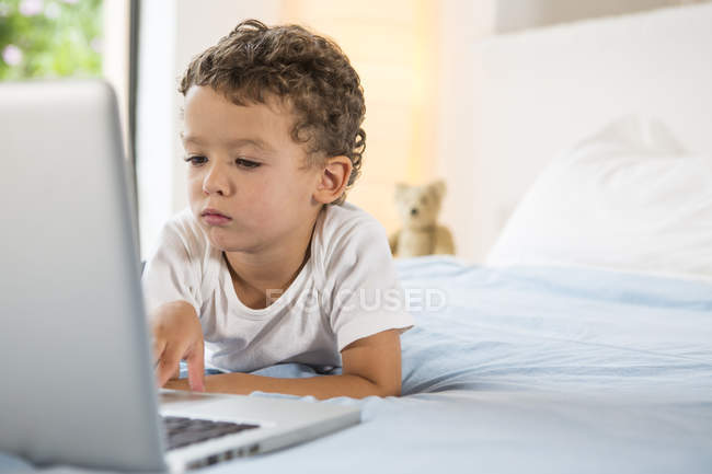 Niño jugando juegos en el ordenador portátil en la cama - foto de stock