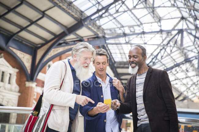 Три дорослі чоловіки на вокзалі, дивлячись на смартфон — стокове фото