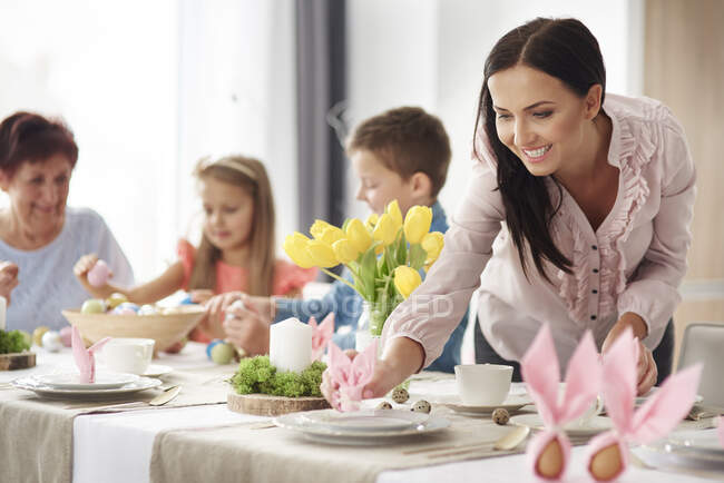 Mulher e família preparando configurações de lugar na mesa de jantar de Páscoa — Fotografia de Stock