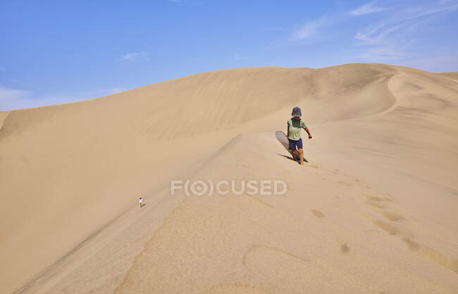 Menino com sandboard em dunas de areia, Ica, Peru — Fotografia de Stock