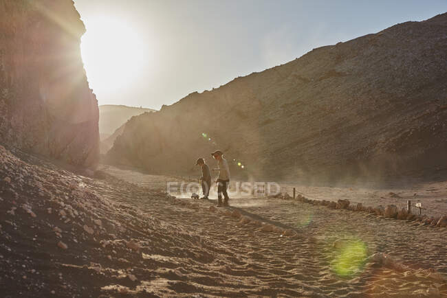 Мальчик и его брат тянут игрушечные грузовики вдоль пустынной тропы, Атакама, Чили — стоковое фото