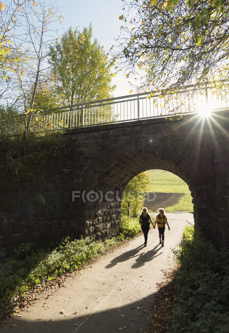 Madre e hija caminando por debajo del puente ferroviario, Mehren, Rheinland-Pfalz, Alemania - foto de stock