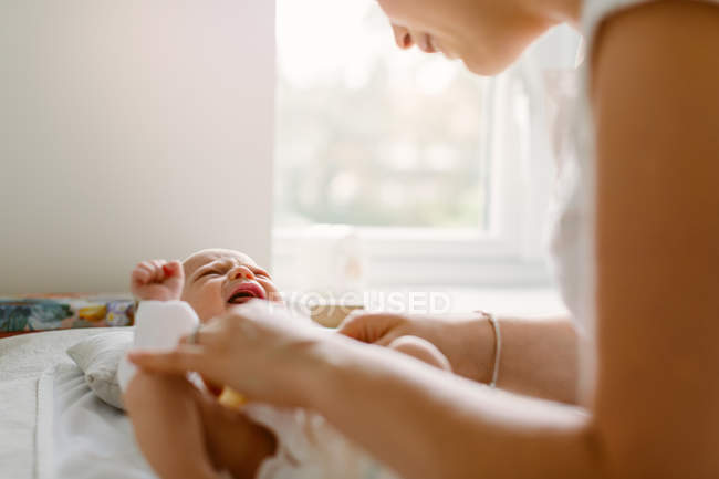 Mujer joven cambiando pañal de hija bebé en la cama - foto de stock