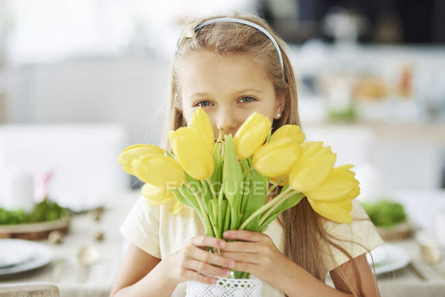 Retrato de niña sosteniendo y escondiéndose detrás de tulipanes amarillos - foto de stock
