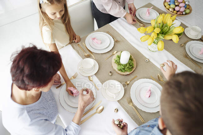 Vista aérea de la abuela y la familia preparando la mesa de comedor de Pascua - foto de stock