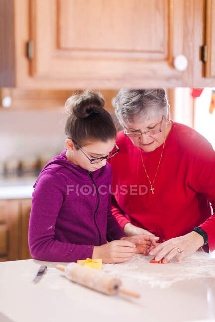 Chica y abuela usando cortador de galletas en la masa en el mostrador de la cocina - foto de stock