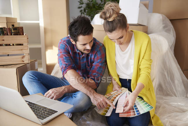 Jeune couple à la maison regardant des échantillons de peinture — Photo de stock