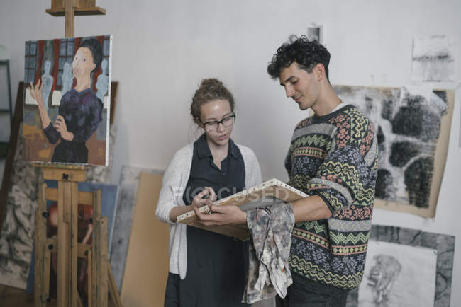 Artista masculino y cliente femenino mirando lienzo en estudio de artista - foto de stock