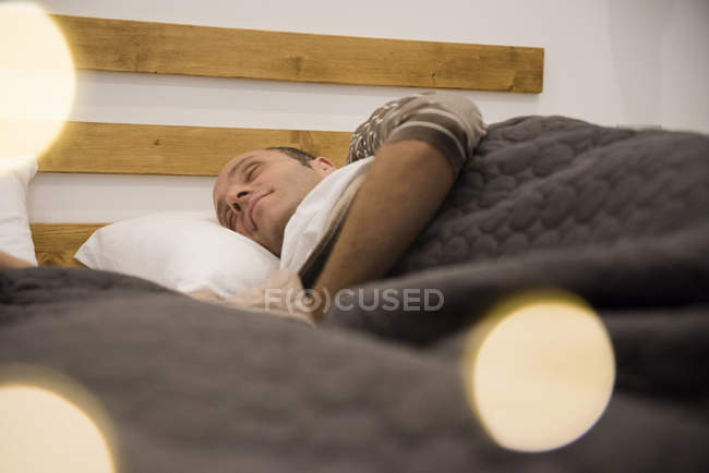 Зрелый мужчина спит под одеялом в постели — стоковое фото