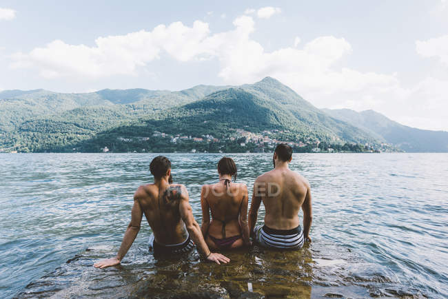 Rear view of three friends sitting in lake Como, Como, Lombardy, Italy — Stock Photo