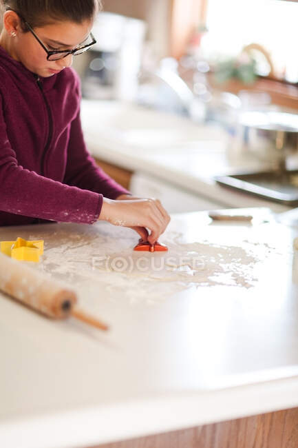 Chica usando cortador de galletas en la masa en el mostrador de cocina - foto de stock