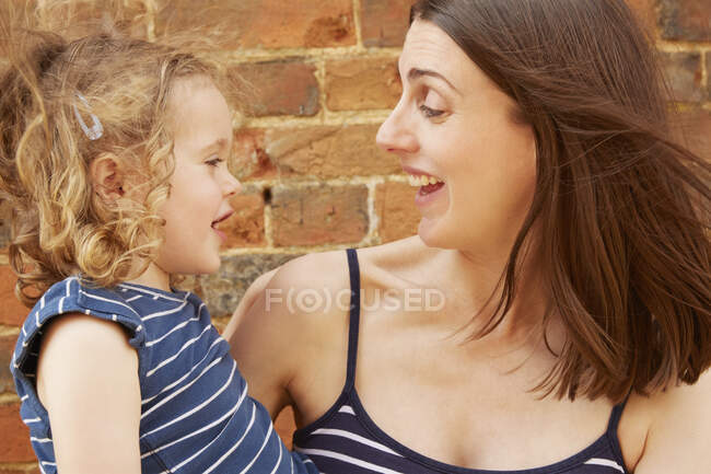 Linda chica y riendo madre por pared de ladrillo - foto de stock