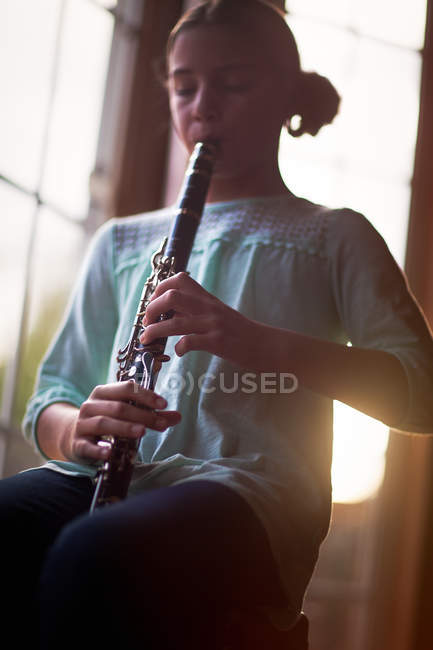 Portrait of girl sitting and playing on clarinet — Stock Photo