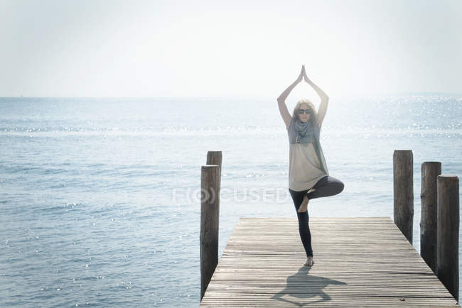Woman on pier balancing on one leg in yoga pose — Stock Photo