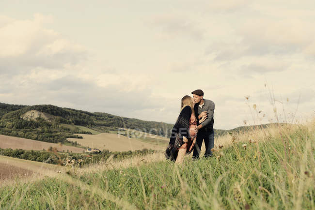 Романтична вагітна пара цілується на сільському схилі пагорба — стокове фото