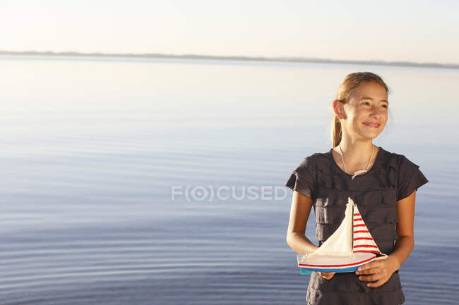 Junges Mädchen steht am Wasser und hält Spielzeugboot in der Hand — Stockfoto