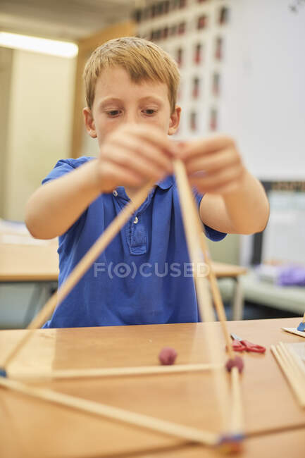 Colegial haciendo modelo de pelota y palo en el aula en la escuela primaria - foto de stock