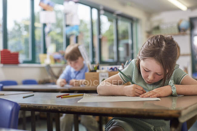 Colegiala escribiendo en clase en la escuela primaria - foto de stock
