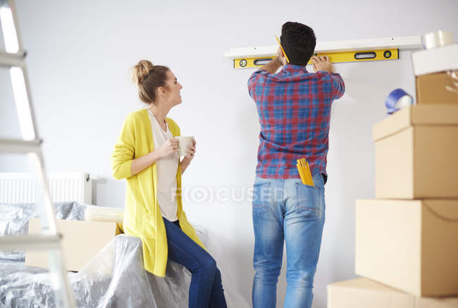 Young couple at home and man checking shelf with level — Stock Photo