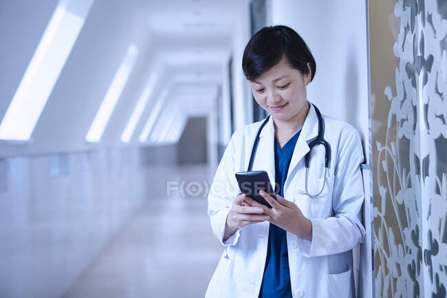 Médico no corredor do hospital encostado à parede usando smartphone — Fotografia de Stock