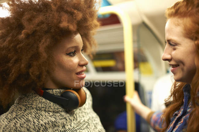 Dos mujeres jóvenes en el tren del metro sonriendo entre sí - foto de stock