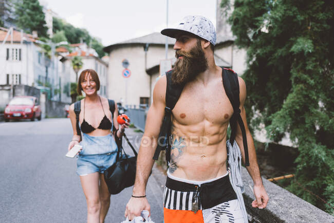 Parejas jóvenes en trajes de baño y mochilas paseando en Como, Lombardía, Italia - foto de stock