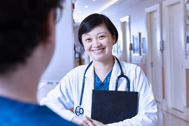 Médico en el hospital charlando con colega sonriendo - foto de stock