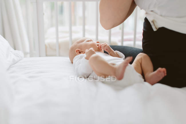 Young woman sitting on bed with baby daughter — Stock Photo