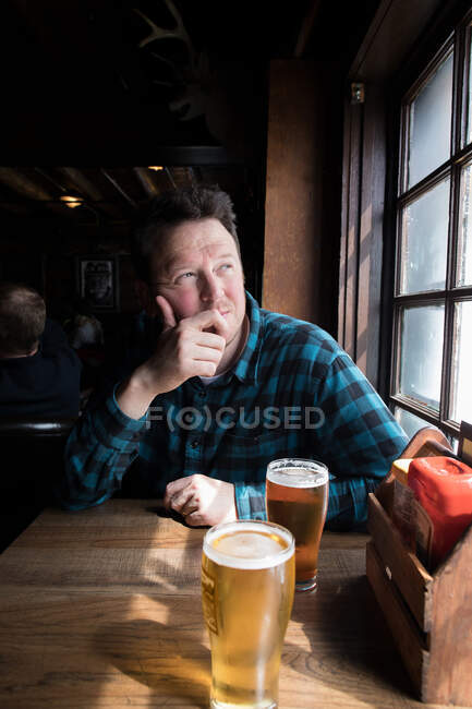 Чоловік пив, дивлячись з вікна — стокове фото