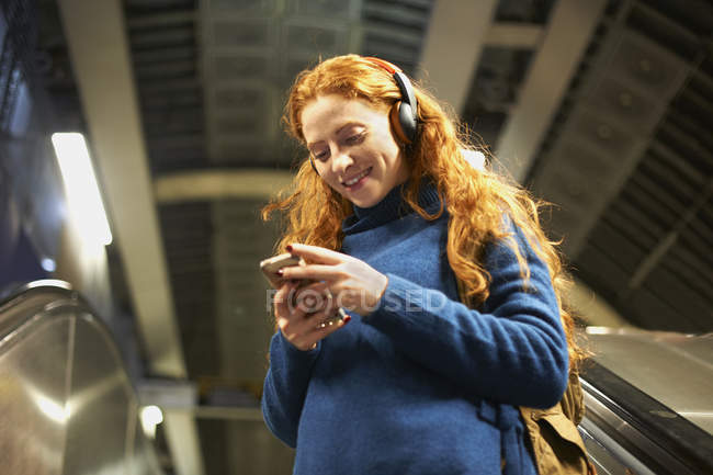 Jeune femme sur escalator regardant smartphone — Photo de stock