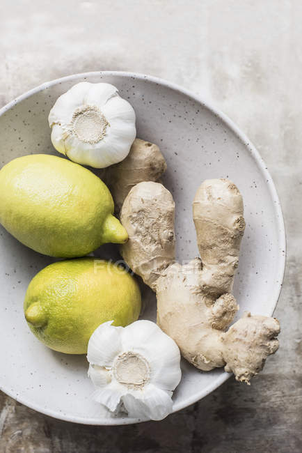 Ginger roots with lemons and garlic in a ceramic bowl, close-up top view — Stock Photo