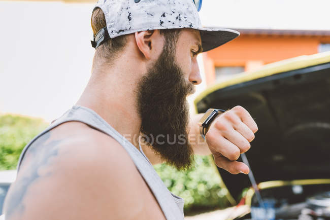 Young man making smartwatch phone call beside car — Stock Photo