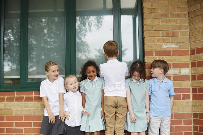 Colegialas y niños de pie en una fila fuera del edificio de la escuela primaria, retrato - foto de stock