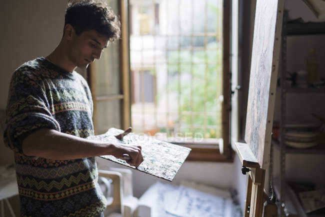 Artista masculino aplicando tinta a óleo na paleta em estúdio de artista — Fotografia de Stock