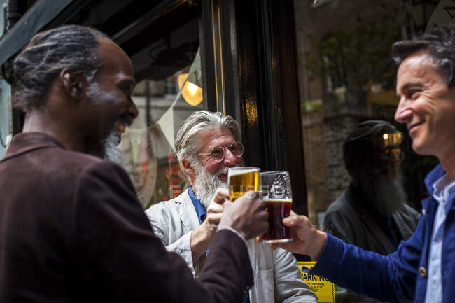Três homens maduros, em pé fora do pub, segurando copos de cerveja, fazendo um brinde — Fotografia de Stock