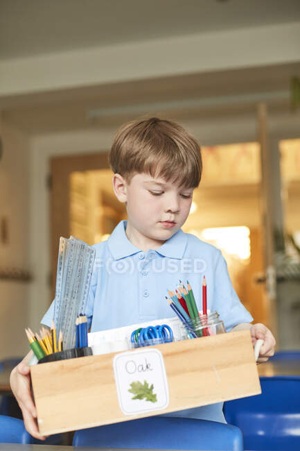 Schoolboy carrying box of pencils in classroom at primary school — Stock Photo