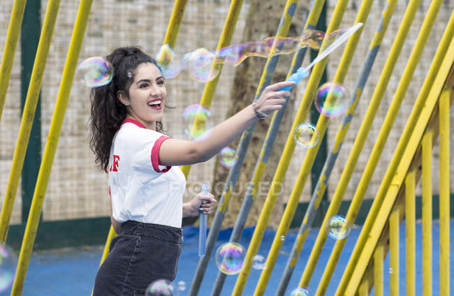 Giovane donna nel parco giochi facendo bolle con bacchetta bolla — Foto stock