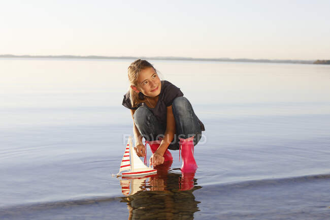 Chica joven flotante juguete barco en el agua - foto de stock