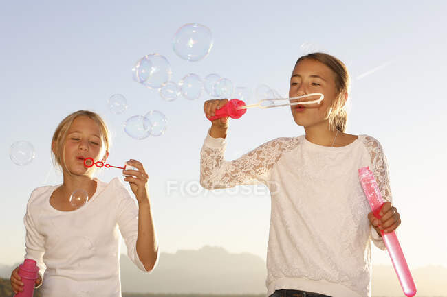 Two young girls, outdoors, blowing bubbles — Stock Photo