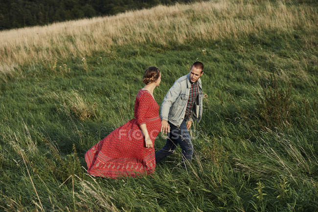 Беременная пара, идущая рука об руку в поле — стоковое фото