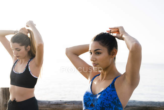 Дві молоді жінки тренуються на пляжі і зав'язують волосся хвостами — стокове фото