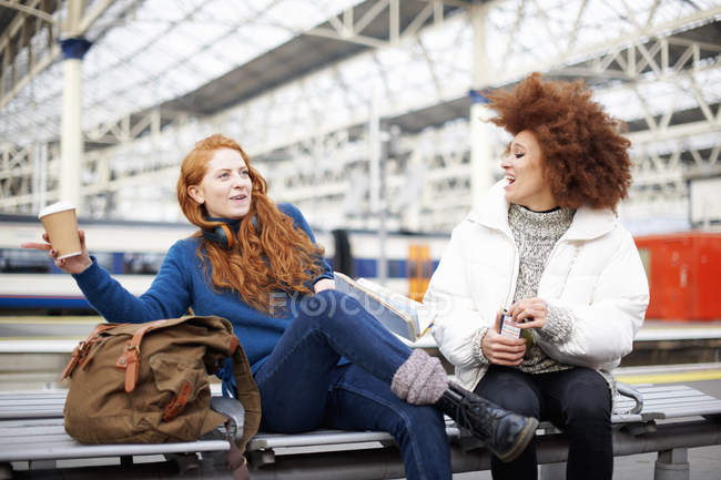 Female friends sitting on bench at train station platform — Stock Photo