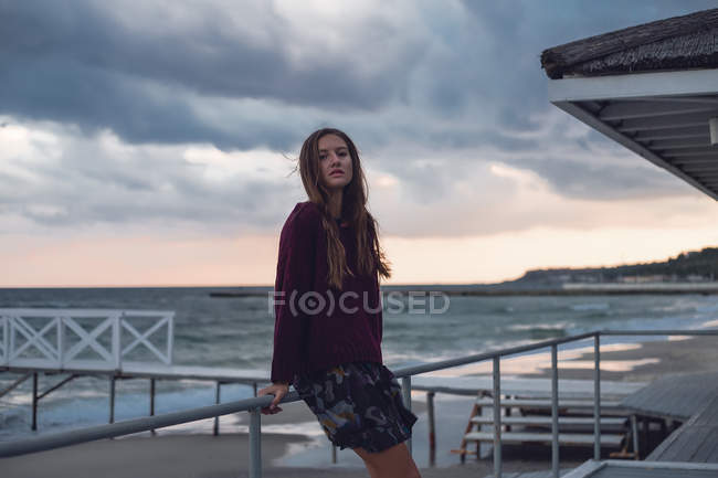 Portrait de jeune femme appuyée contre la jetée de la plage au crépuscule — Photo de stock