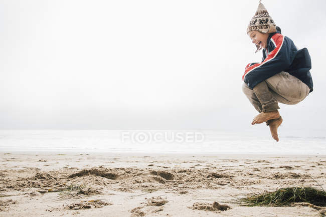Young boy on beach jumping mid air — Stock Photo