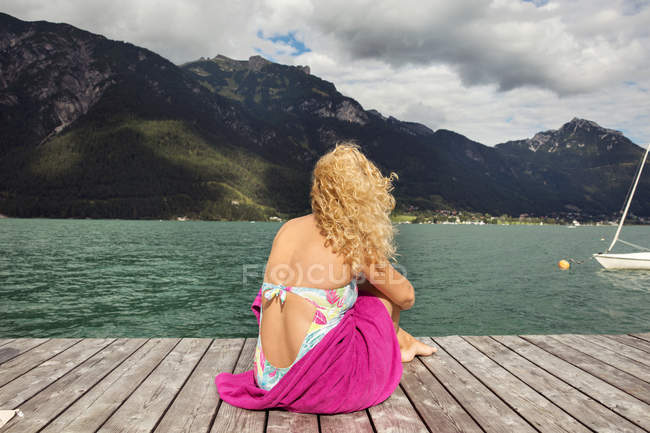 Rückansicht einer Frau, die auf einer Seebrücke sitzt und wegschaut, innsbruck, tirol, Österreich, europa — Stockfoto