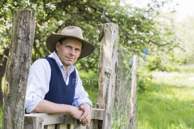 Portrait of man in hat leaning against wooden gate — Stock Photo